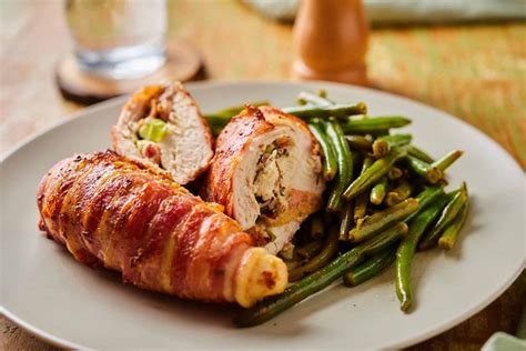 A White Plate Topped With Green Beans And Wrapped Chicken Meat Next To