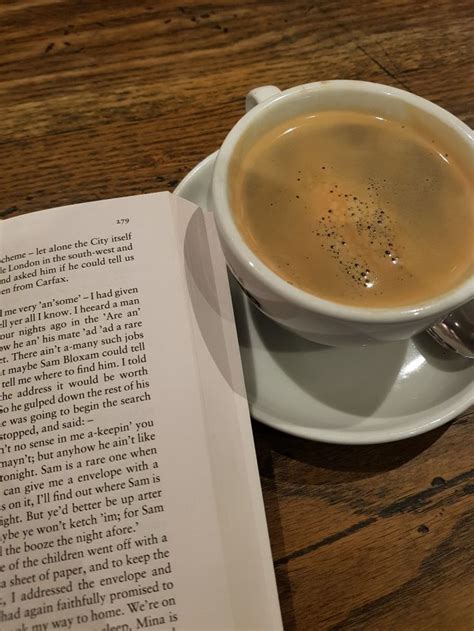 A Cup Of Coffee Sitting On Top Of A Saucer Next To An Open Book