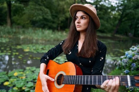 Premium Photo Cute Brunette Girl In A Hat Is Playing Acoustic Guitar And Enjoying Music In The