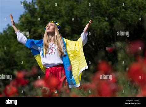 Eine junge blonde Ukrainerin steht auf einem Feld mit roten Mohnblumen und hält Flagge der