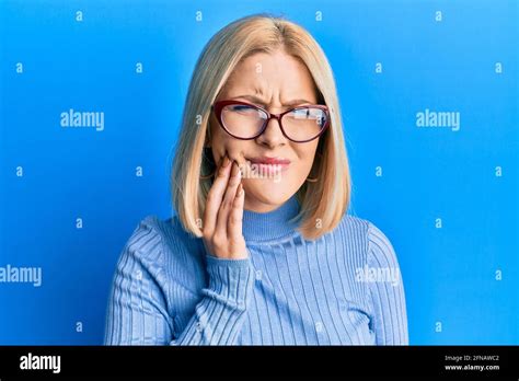 Jeune femme blonde portant des vêtements décontractés et des lunettes touchant la bouche avec la