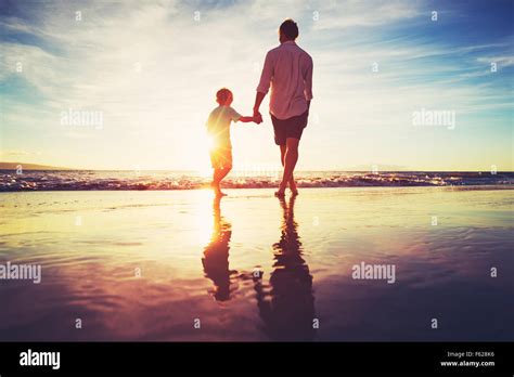 Father And Son Holding Hands Walking Together On The Beach At Sunset