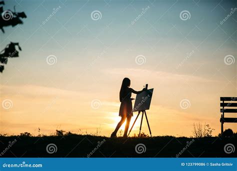 La Silueta De Un Artista Lady De La Muchacha Del Blonde Pinta Una Pintura En La Lona Con La