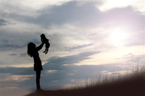 Silhouettes Of Mather And Little Daughter Walking At Sunset Stock Photo