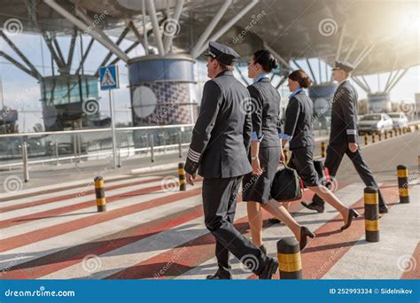 Two Flight Attendants And Male Pilots Walking In A Row While Crossing