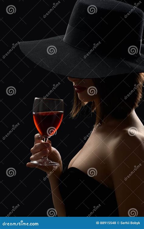 Elegant Mysterious Woman In A Hat Holding A Glass Of Red Wine On Stock