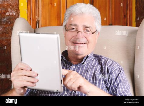 Portrait Of An Old Man Using Digital Tablet And Sitting On Couch