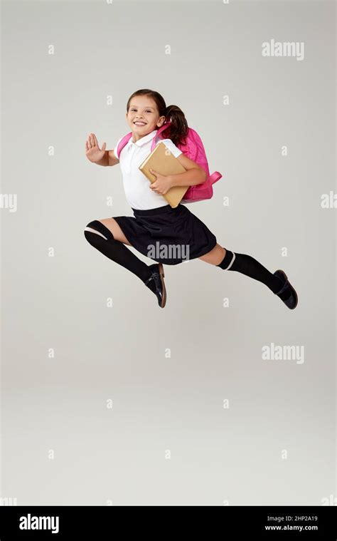 Happy Schoolgirl Jumping Up With Pink Backpack Isolated On Gray