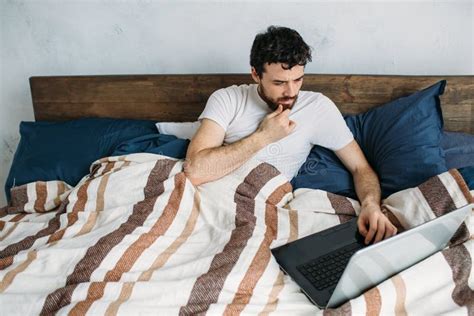 Bearded Man Reading A Big Book Lying In His Bedroom Stock Image