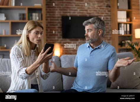 Sad Mature Caucasian Wife Shows Smartphone To Shocked Husband Man Suffers From Gadget Play