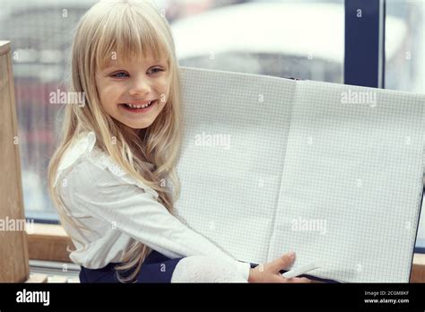 belle petite fille blonde sourit et montre un bloc notes déplié avec des feuilles vierges mise