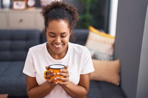 African American Woman Drinking Coffee Sitting On Sofa At Home Stock