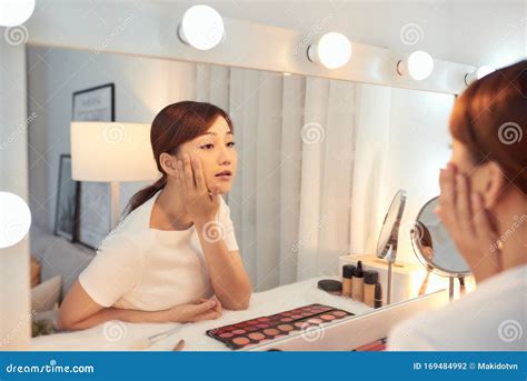 Focused Beautiful Young Asian Woman Looking At Herself In The Mirror