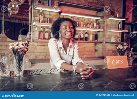 Smiling African American Bartender Leaning On Bar Counter With Clasped