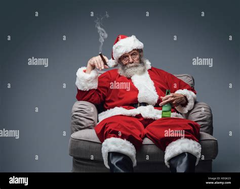 Bad Santa celebrating Christmas at home alone, he is smoking a cigar and drinking beer Stock ...