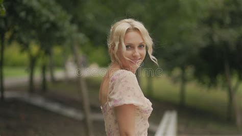 Middle Aged Blonde Woman In Pink Dress Flirting And Smiling At Camera In Park Stock Footage