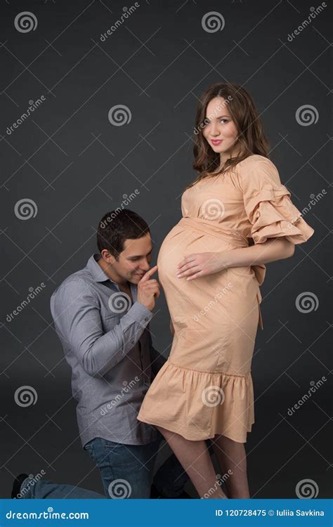 Pregnant Woman In A Beige Dress With Her Husband Standing On The Gray Background Stock Image