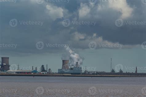 Industrial Landscape With Smokestacks Emitting Smoke Over A Body Of