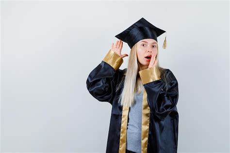 졸업 가운에 입 근처에 손을 잡고 뭔가를 듣고 귀 근처에 손을 잡고 금발 소녀 무료 사진