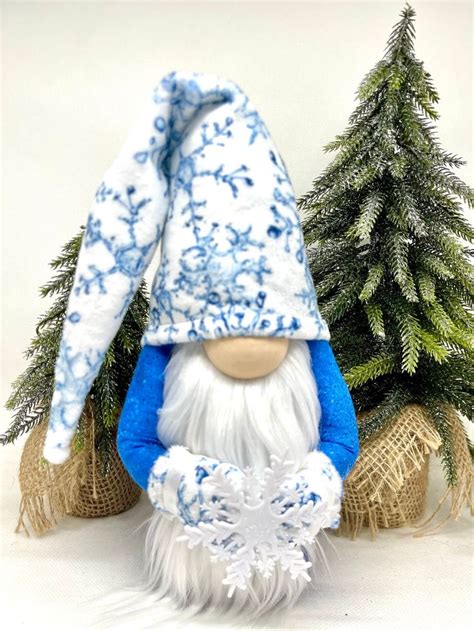 A Blue And White Gnome Figurine Sitting In Front Of Two Small Christmas