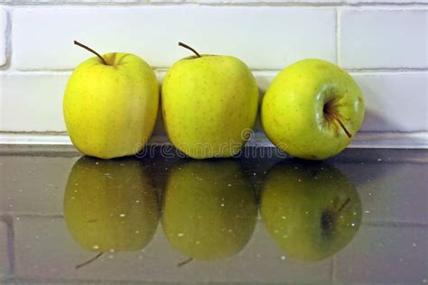 Three Golden Apples And Reflection On The Countertop Stock Image