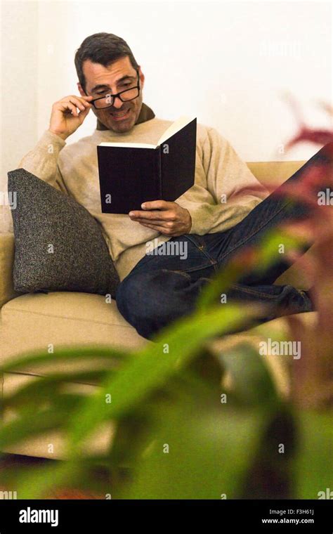 Mature Man Sitting On Sofa Wearing Eye Glasses Reading A Book Stock Photo Alamy