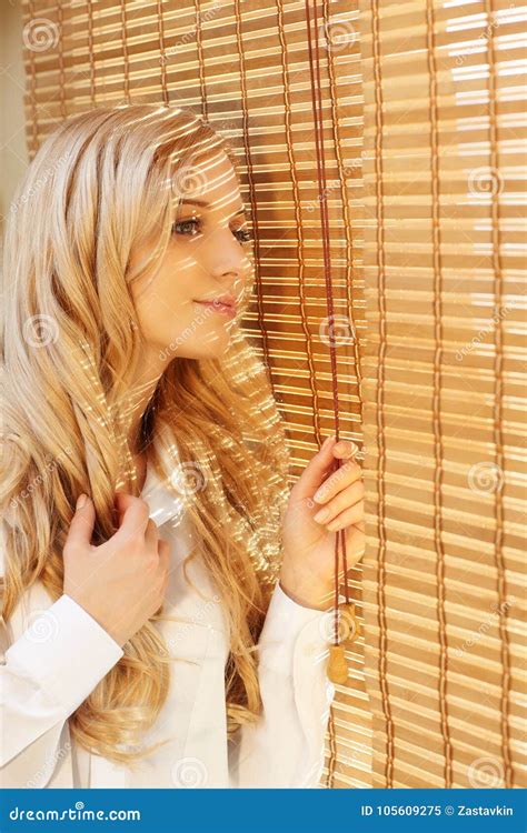 Young Happy Woman Looking Out The Window Through The Blinds Stock Image