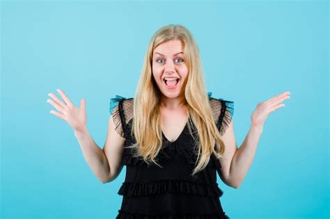 Une Fille Blonde Heureuse Regarde La Cam Ra En Ouvrant Grand Ses Mains Sur Fond Bleu Photo