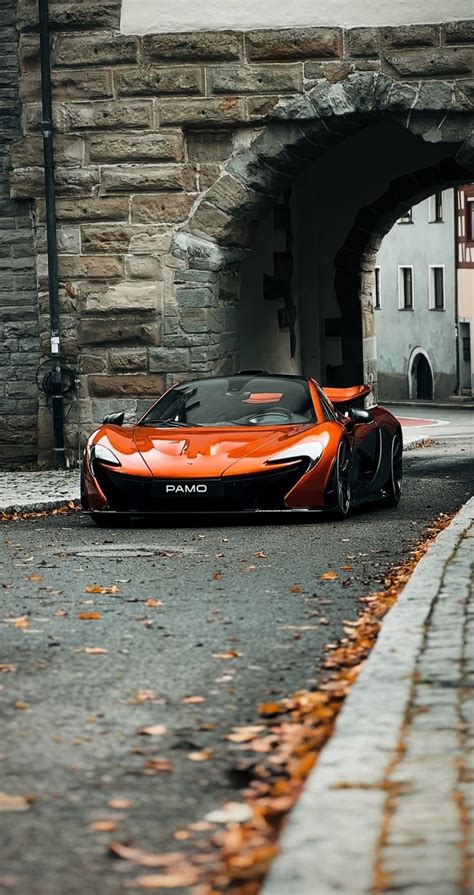 An Orange Sports Car Parked In Front Of A Stone Tunnel With Leaves On