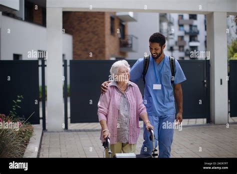 Caregiver Walking With Senior Woman Client In Front Of Nurishing Home