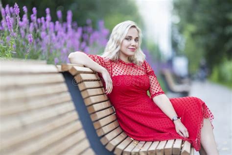 Une Jeune Femme Assise Sur Un Banc Dans Un Parc En Fleurs Belle Blonde Souriante Dans Une Robe