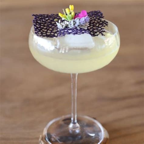 A Small Glass Filled With A Drink And Garnished With Flowers On The Rim