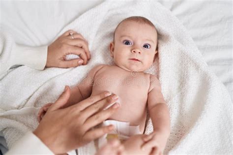 Adorable Caucasian Baby Lying On Bed Applying Cream On Body Skin At