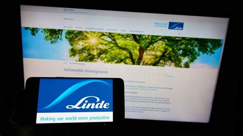 Person Holding Cellphone With Logo Of Chemical Company Linde Plc On Screen In Front Of Webpage