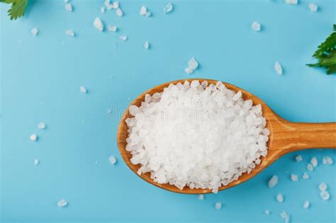 Sea Salt In A Wooden Spoon On Large Salt Crystals With Greens On A Blue