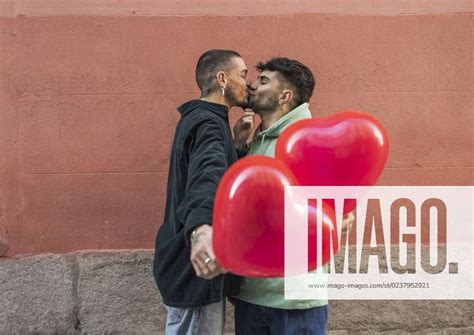 Affectionate Gay Couple Kissing With Red Heart Shape Balloon In Front