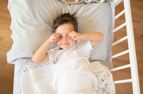 Lindo niño caucásico frotándose los ojos por la mañana en la cama foto