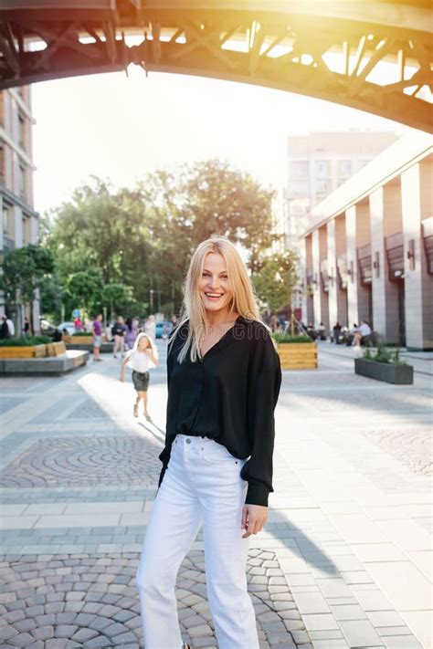 Fröhliche Attraktive Junge Blonde Frau in Weißer Hose Sich Kamera Anschaut Stockfoto