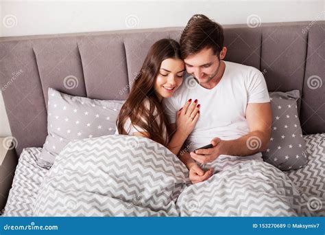 Smiling Young Couple Taking Selfie Together In Bedroom Stock Image