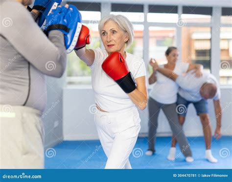 Mature Woman With Her Trainer At Gym Woman Wearing Boxing Gloves Exercise And Punch To Pads For