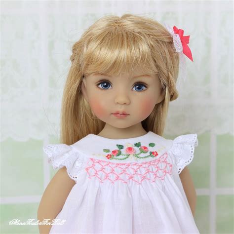 A Doll With Blonde Hair And Blue Eyes Is Wearing A White Dress That Has