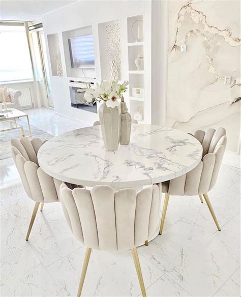 A Marble Dining Table Surrounded By Beige Chairs And Vases With Flowers