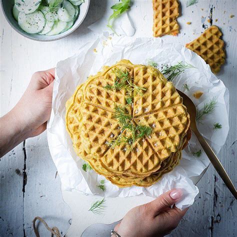 Two Hands Holding Waffles With Cucumber Slices On The Side