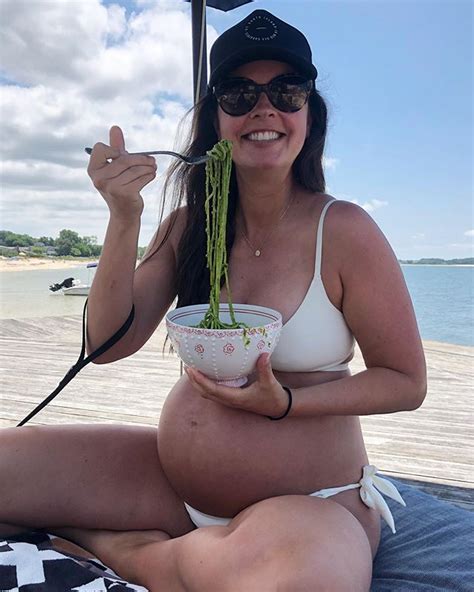 A Pregnant Woman Holding A Bowl Of Food On Her Lap And Smiling At The