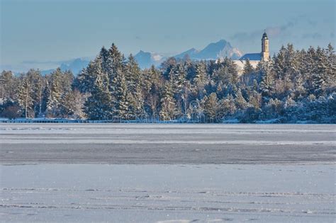 Frozen Mountain Lake With Ice Skaters And A Church In The Background