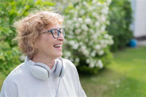 An Elderly Caucasian Woman Walks In A Park And Listens To Music