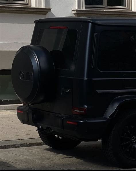 A Black Jeep Parked On The Street Next To A White Building With Windows