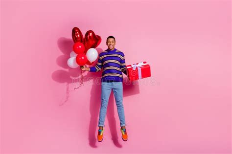 Full Length Photo Of Excited Funky Man Wear Striped Sweater Jumping Rising Present Box Balloons