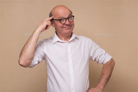 Mature European Man With Beard Holds Fingers On Temple Having Idea