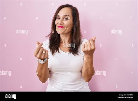 Middle Age Brunette Woman Standing Over Pink Background Doing Money Gesture With Hands Asking